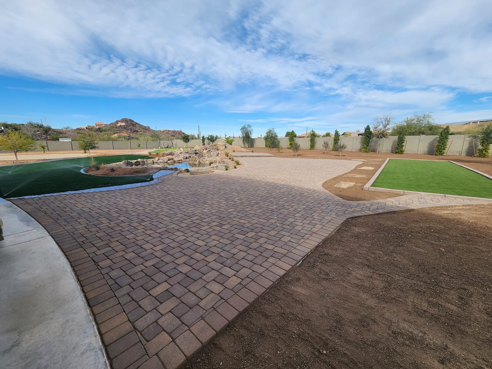 The paver patio seen from the house, with turf lawn, boulder water feature and putting green beyond