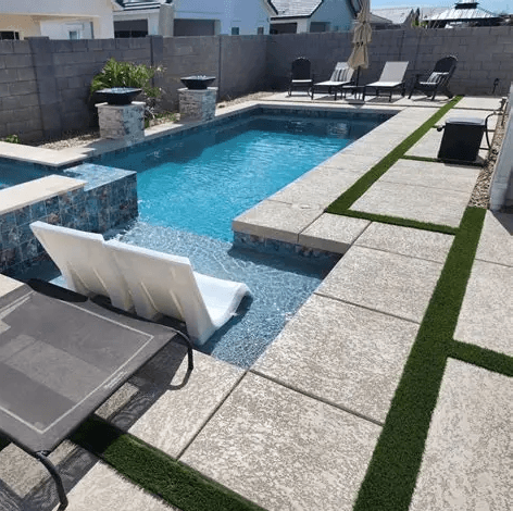 Paver pool deck with turf inlay strips and a stacked-stone water feature